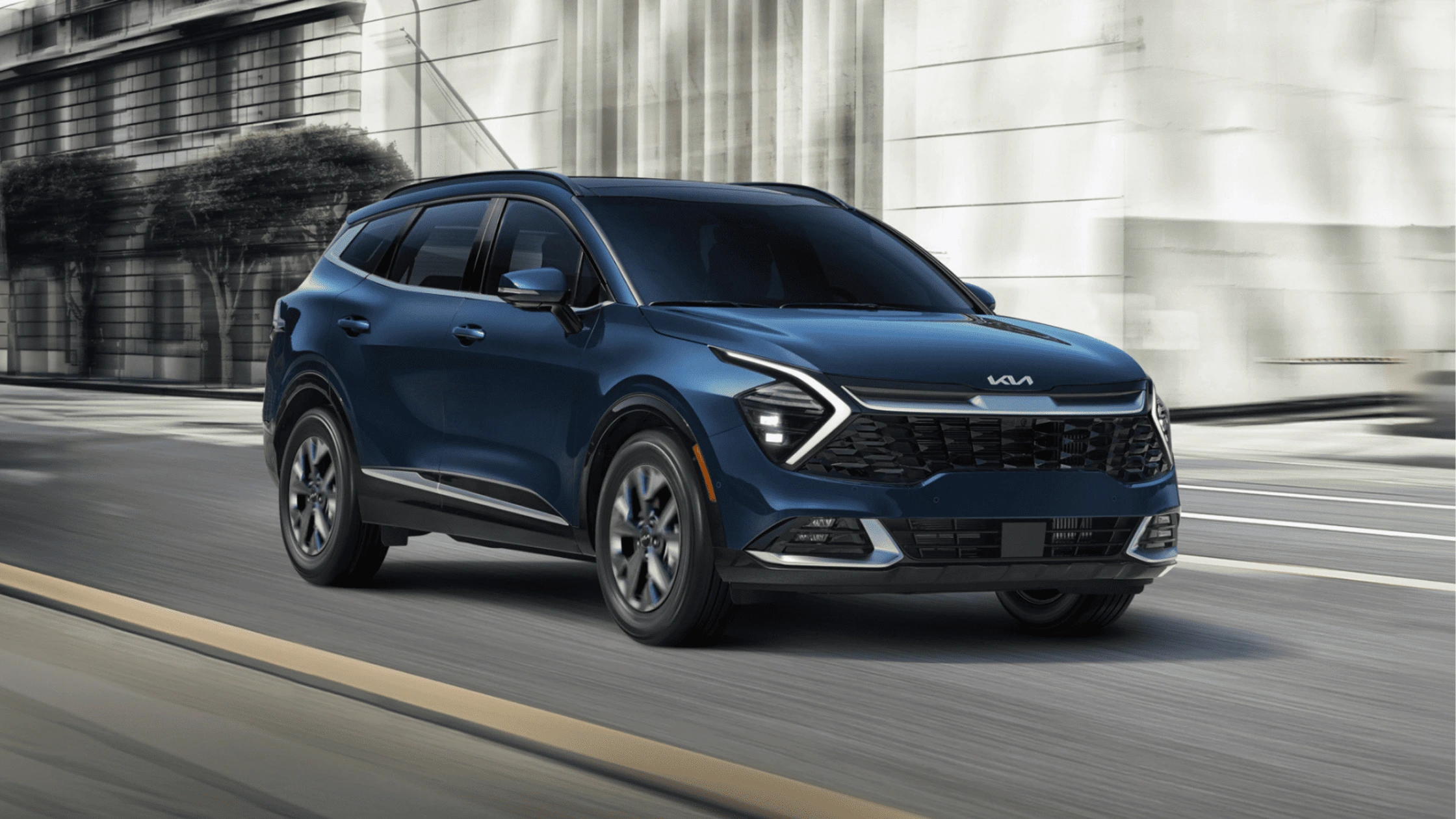 The 2025 Kia Sportage Hybrid in Fort Myers, FL The 2025 Kia Sportage Hybrid in deep blue driving through an urban setting, highlighting its bold front grille and LED lighting.