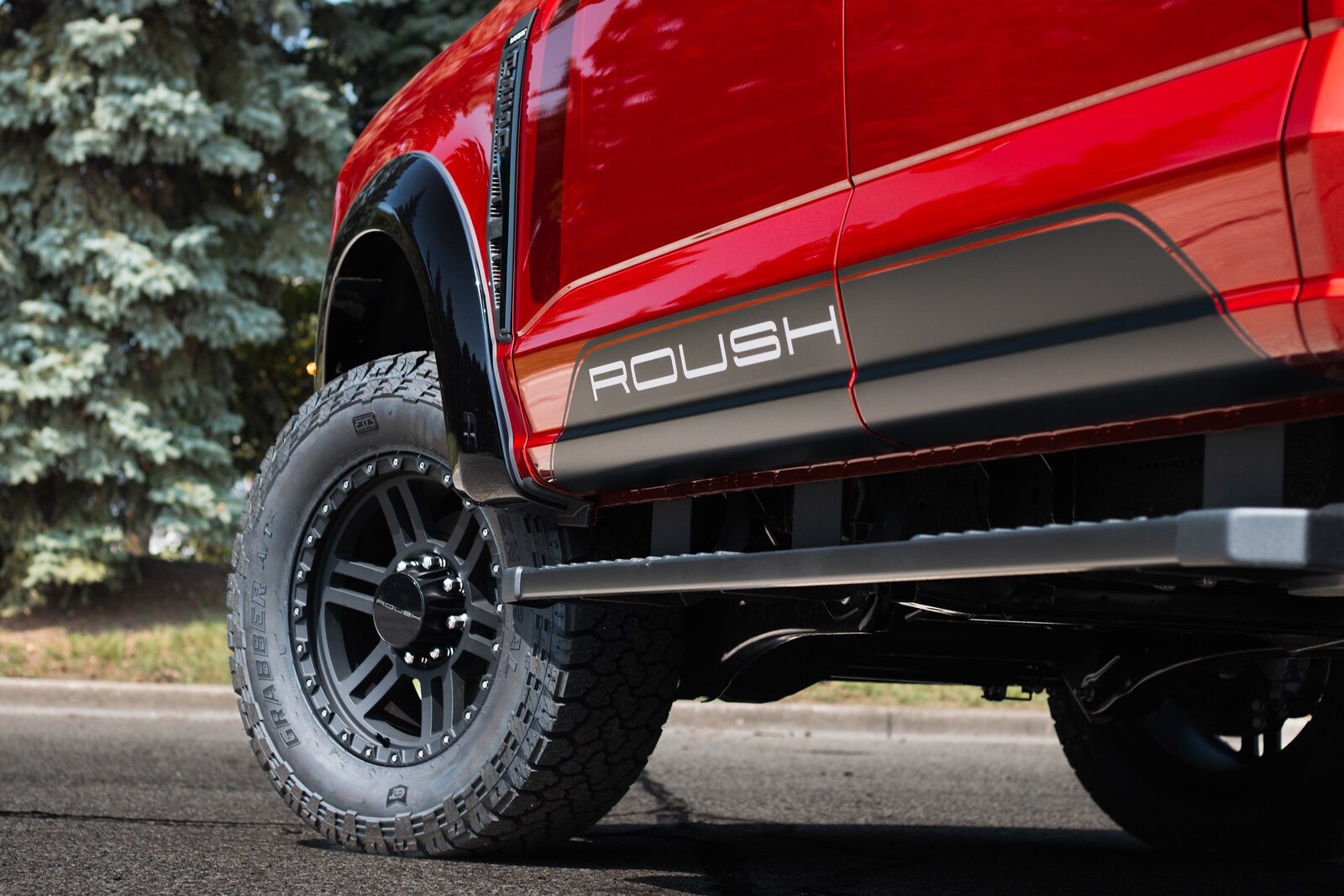 Close-up of ROUSH rocker graphic, black fender flare, and General Grabber A/T tire on a red Super Duty