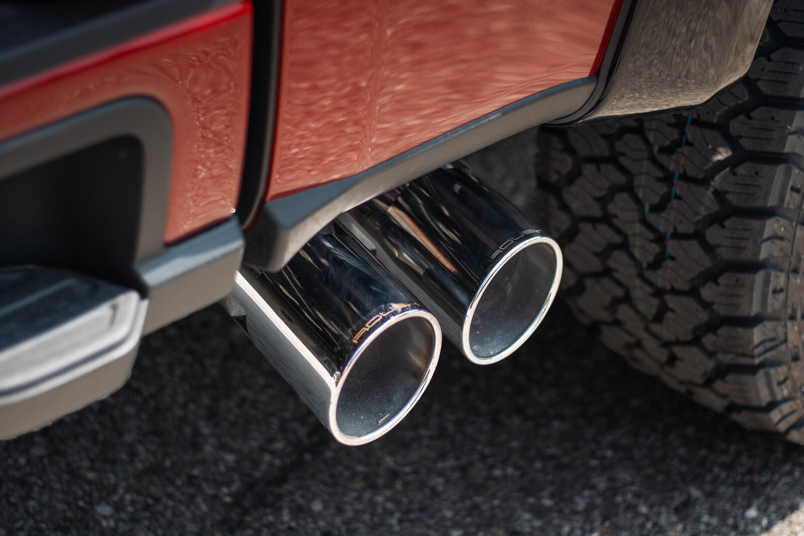 Dual polished exhaust tips under the rear bumper of a red ROUSH Super Duty