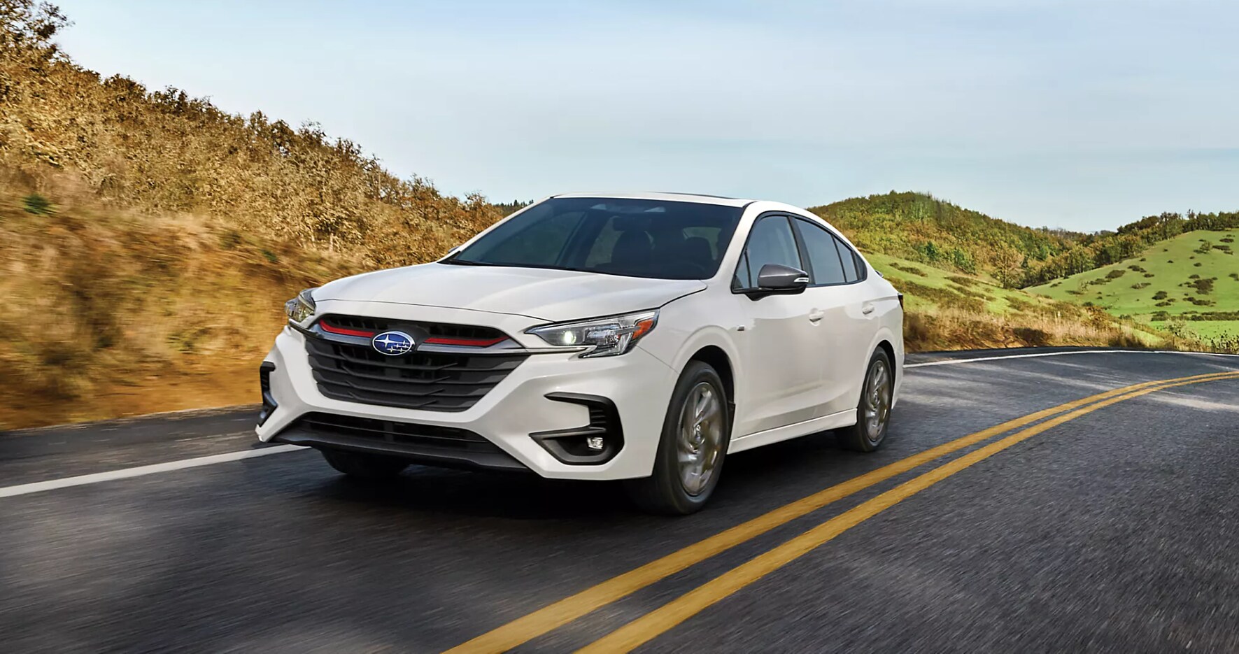 2023-subaru-legacy-1.PNG A white 2023 Subaru Legacy drives on a country road