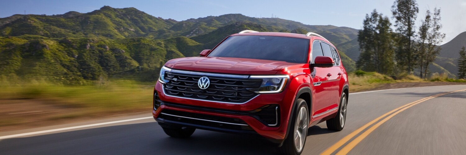 2024 Atlas red 2024 Volkswagen Atlas driving down a scenic road