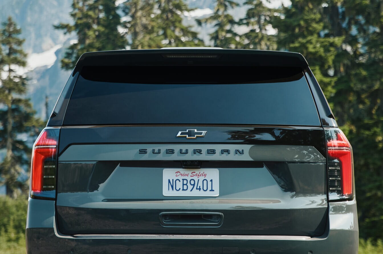 2026 Chevrolet Suburban Z71 in Cypress Green, rear view parked in a mountain forest.