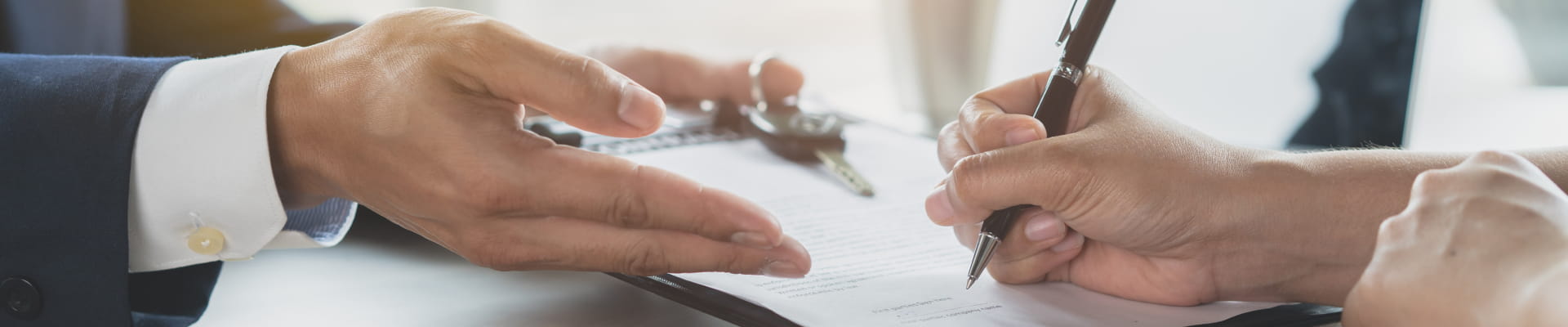 Customer signing paperwork while a representative gestures across the desk, with car keys nearby.