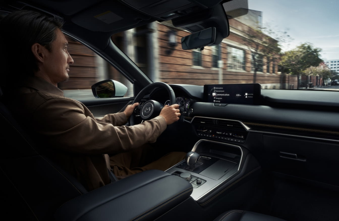 Driver behind the wheel of the Mazda CX-90 with a view of the dashboard and center display.