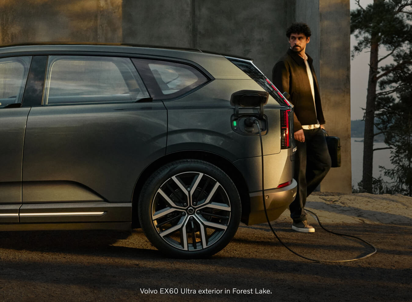 Side profile view of a green Volvo EX60 Ultra charging next to a concrete wall with a man walking past.