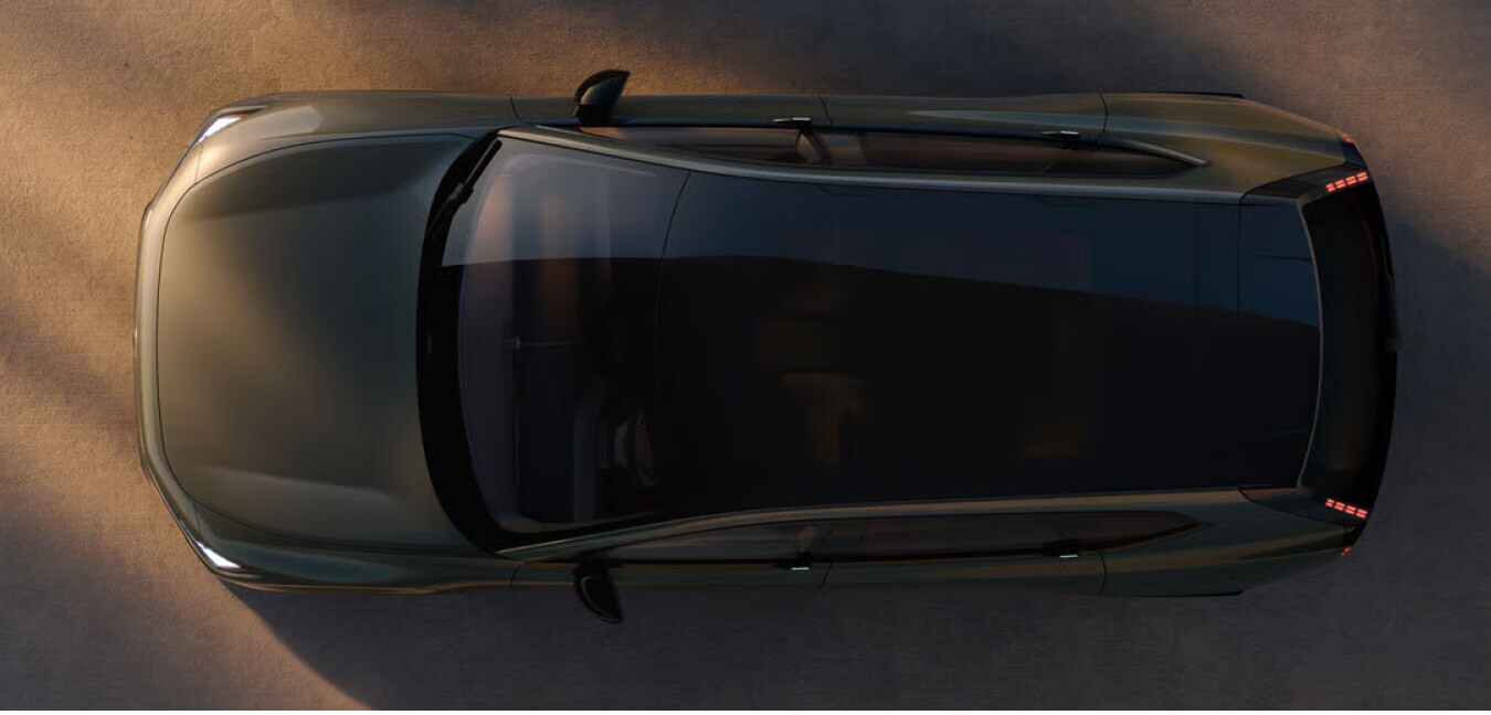 Top-down view of a green Volvo EX60 Ultra highlighting its glass panoramic roof parked on sunlit concrete.