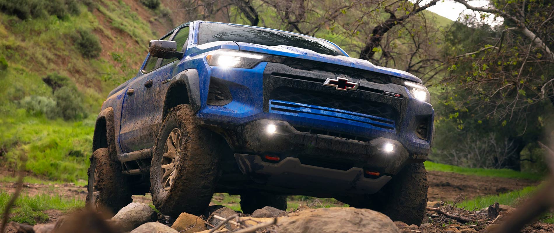 Chevy Colorado For Sale Near Plattsburgh, NY A blue Chevy Colorado driving over rocky terrain in a forest.