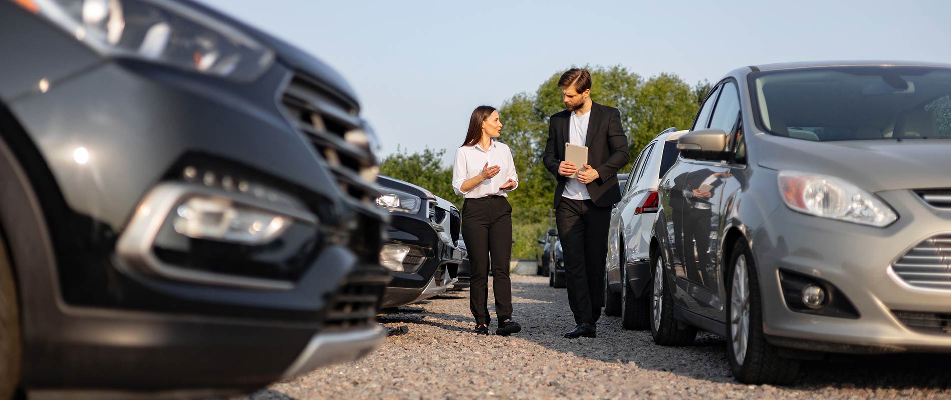 Used Car Dealer Near Plattsburgh A salesperson taking a customer through a row of cars on a dealership lot.