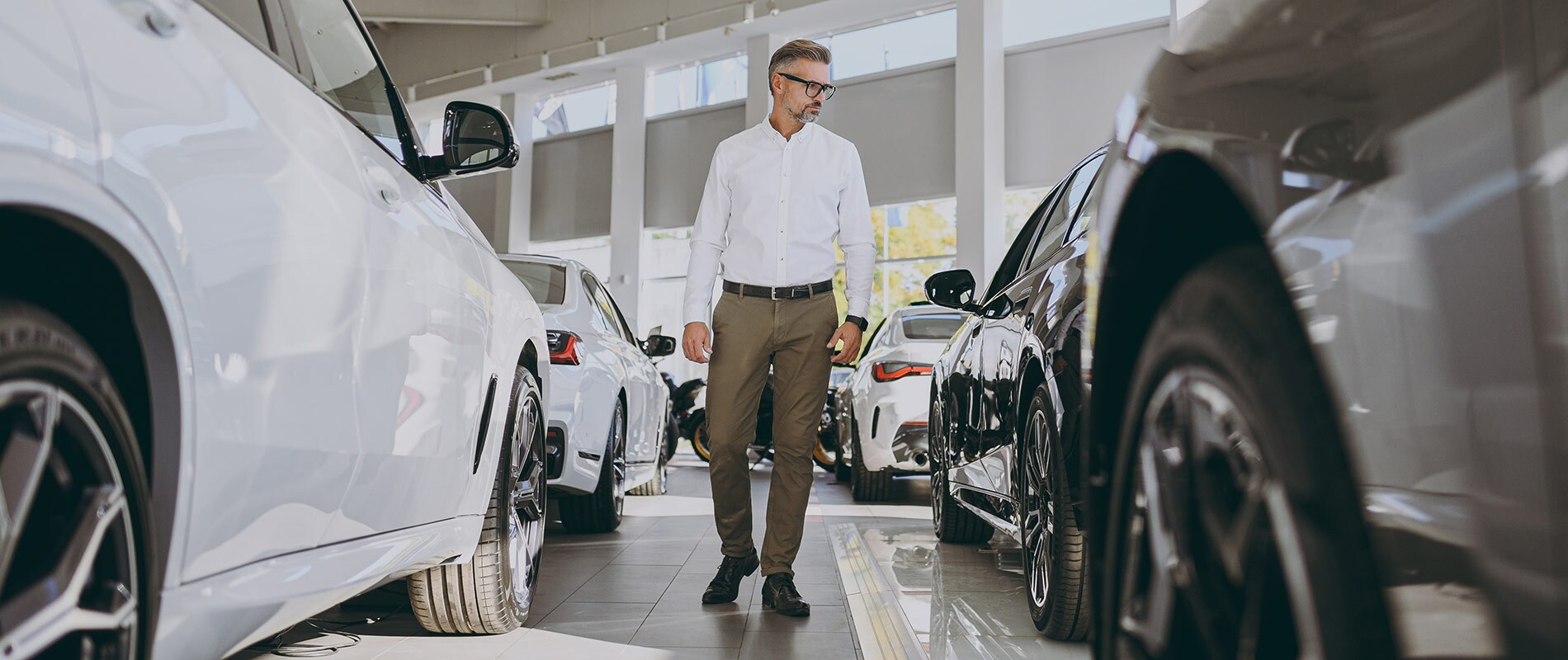 Used Car Dealer Near Malone, NY A man walking down a row of vehicles at an indoor dealership.