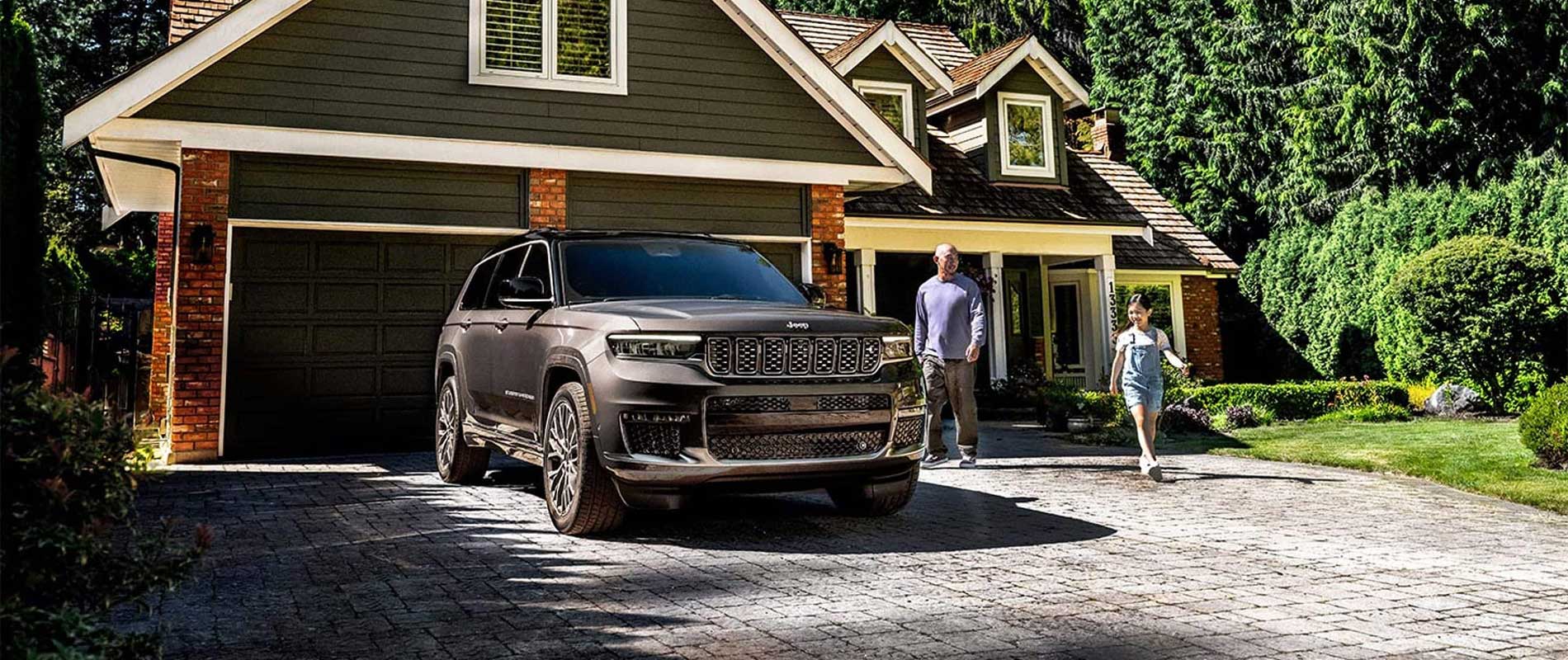 Jeep Dealer Near Colchester A gray Jeep Grand Cherokee parked in a house's driveway with a father and daughter walking towards the vehicle.