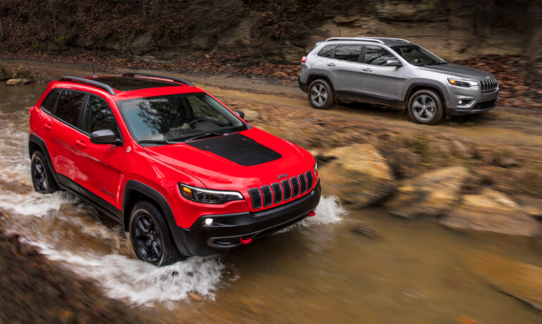 Two Jeep Cherokees driving in the woods by a river