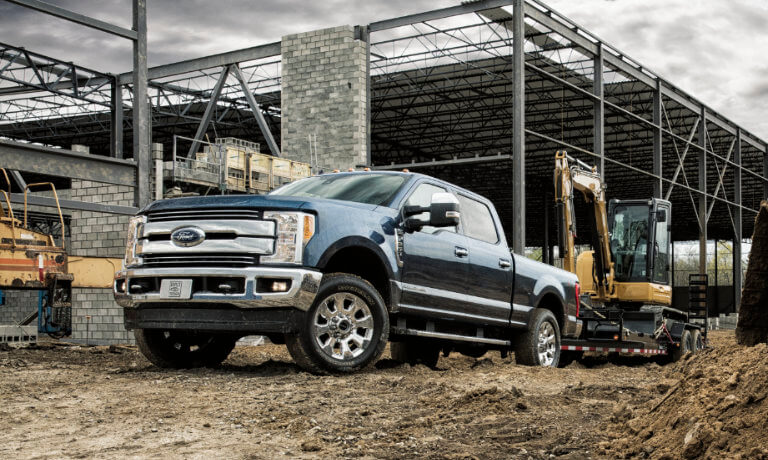 Blue 2019 Ford F-250 hauling machinery on a construction site