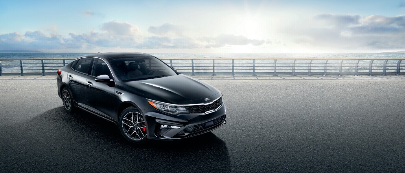 2020 Kia Optima in black parked on a road along the ocean front