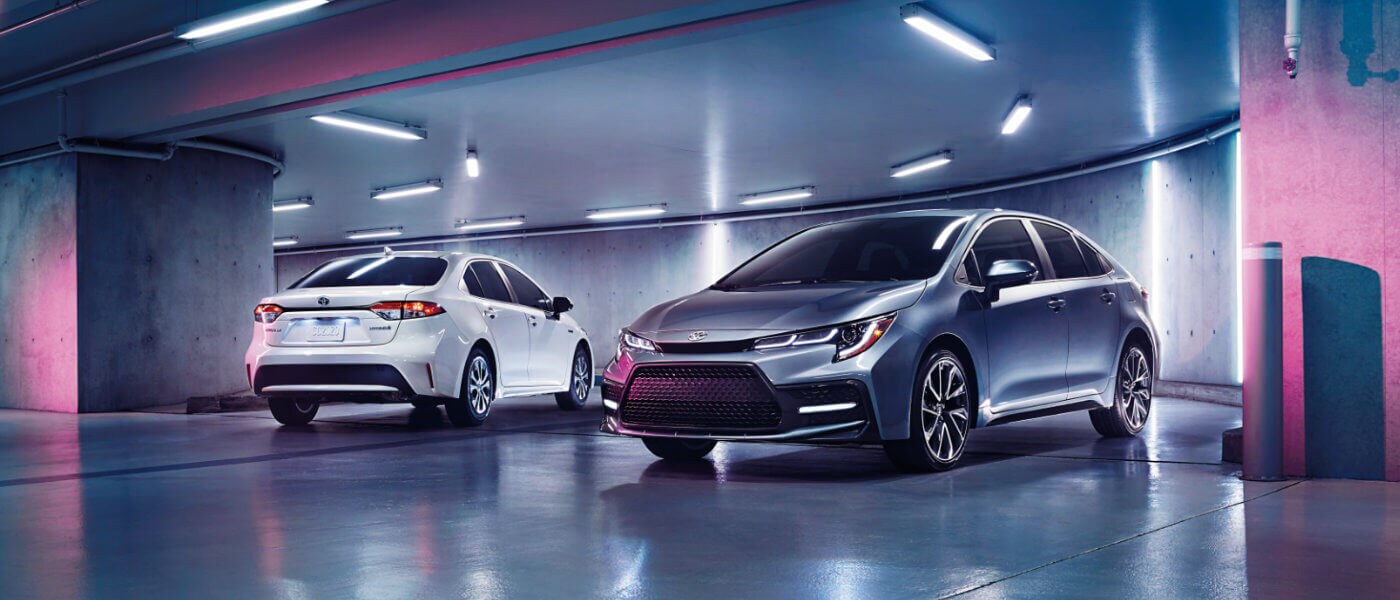 Two Toyota Corollas in white and silver parked in a garage with colorful lights