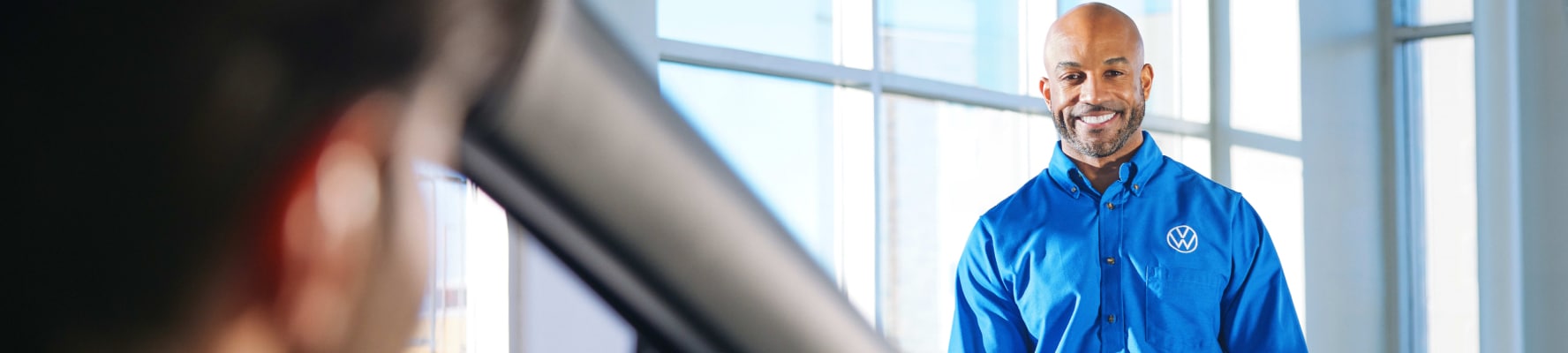 Volkswagen service advisor in blue uniform smiling in dealership showroom