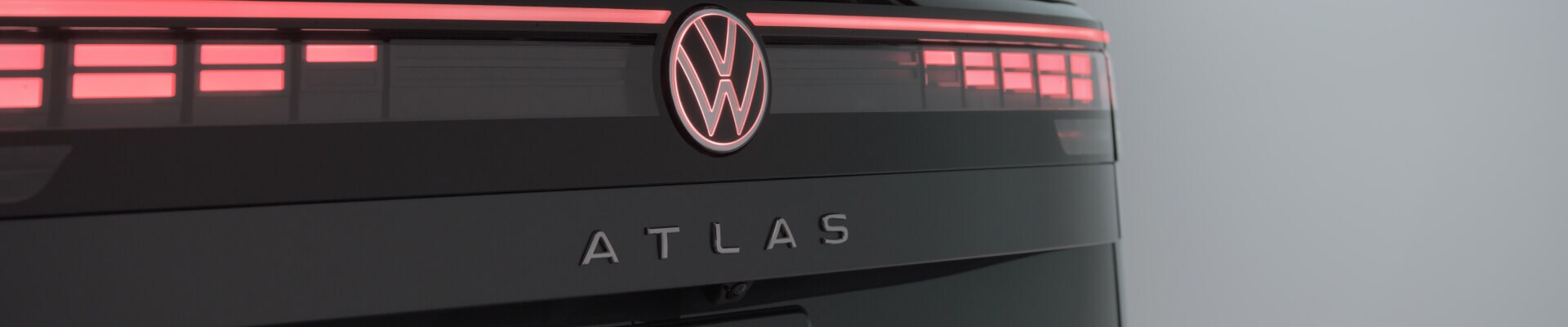 Close-up rear view of a 2027 Volkswagen Atlas SEL Premium R-Line illuminating its logo and tailgate lettering in a studio.