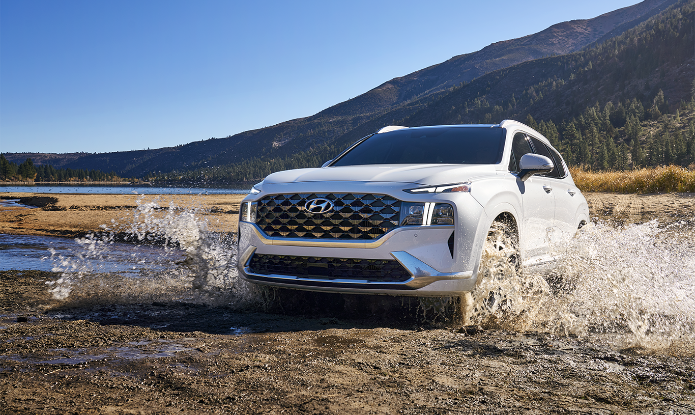 2023 Hyundai Santa Fe at Haddad Hyundai | Front profile of a white 2023 Hyundai Santa Fe driving over a small puddle with views of the mountains in the background