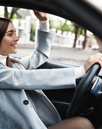Defining GAP Insurance at Haddad Hyundai in Pittsfield, MA | Woman wearing a grey coat and smiling while driving her car with one hand on the steering wheel