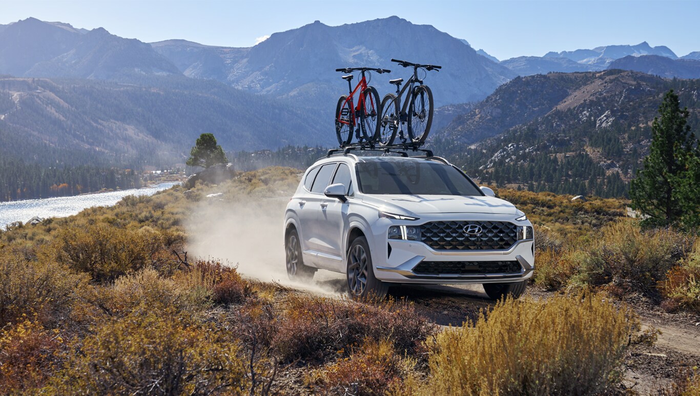 2023 Hyundai Santa Fe at Haddad Hyundai | White 2023 Hyundai Santa Fe driving on dirt road with bike rack on the roof