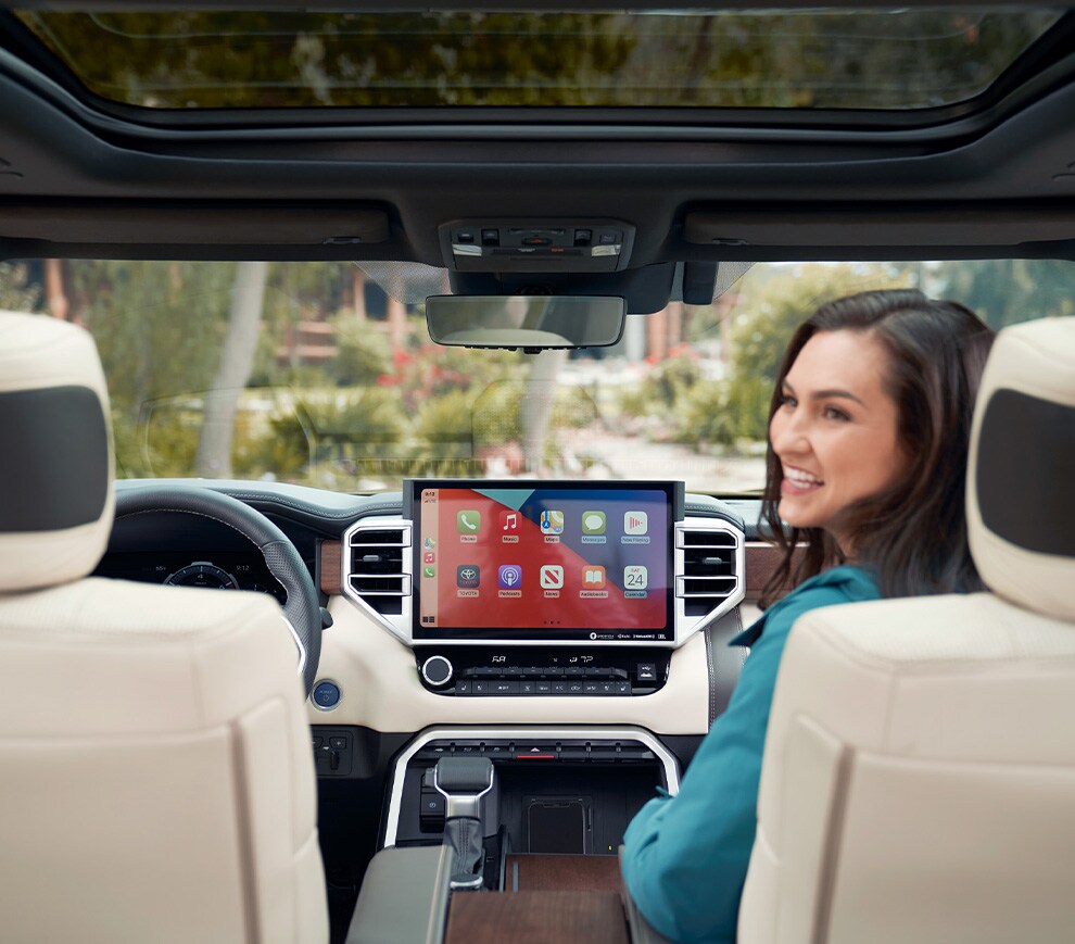 Car Technology Trends at Haddad Toyota in Pittsfield, MA | Woman smiling and sitting in passenger seat of a Toyota Tundra with Apple CarPlay displayed on the touch screen