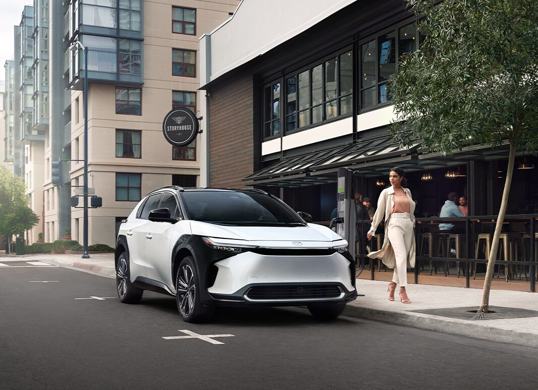 The All-New 2023 Toyota BZ4X at Haddad Toyota in Pittsfield, MA | White 2023 Toyota BZ4X parked on the side of the road with a woman walking by it