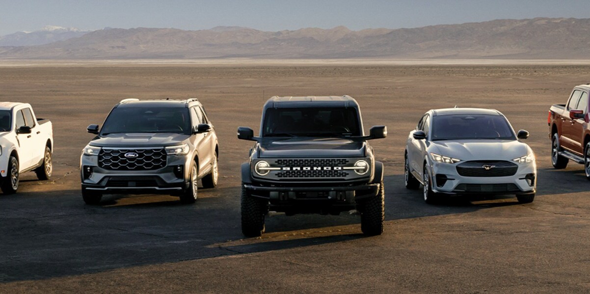 Four Ford vehicles-including the Bronco, F-150, Edge, and Escape-lined up in front of the skyline at sunset, showcasing the full Ford lineup in an desert setting.