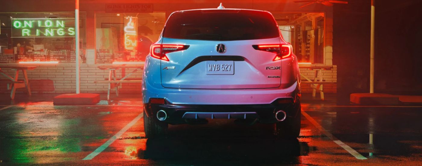 Rear view of a white 2026 Acura RDX parked near a neon lit restaurant.