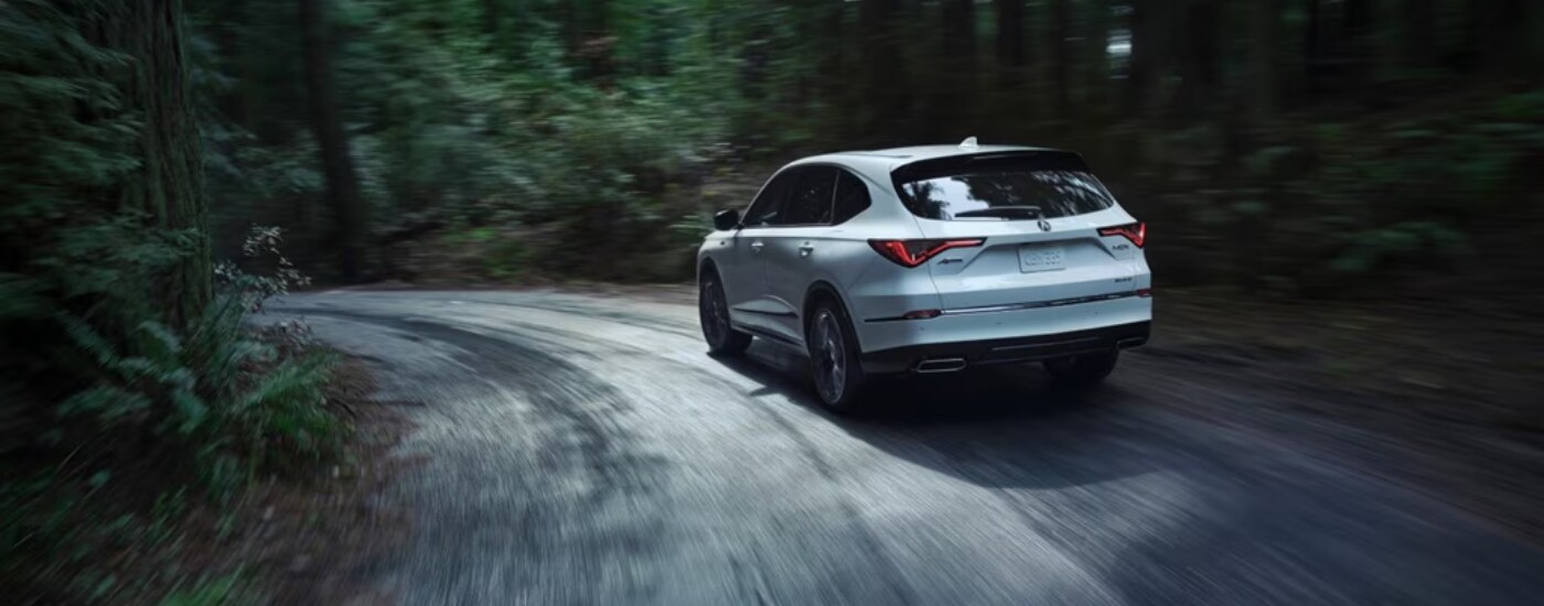 2026%20Acura%20MDX%20-%20bend.png Silver 2026 Acura MDX rounding a bend from the rear