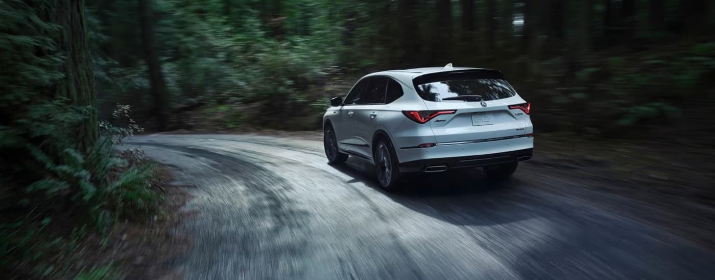 Rear of a white 2026 Acura MDX driving around a bend.