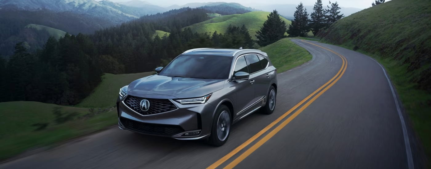 Grey 2026 Acura MDX driving around a bend.