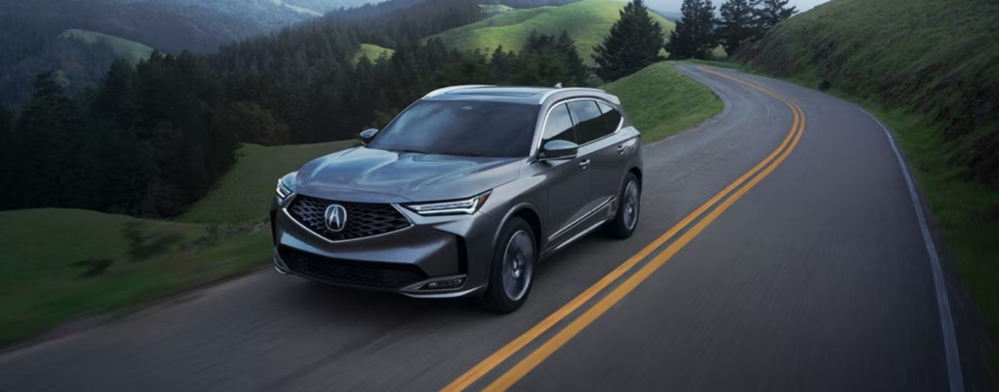 Grey 2026 Acura MDX driving on a paved road.