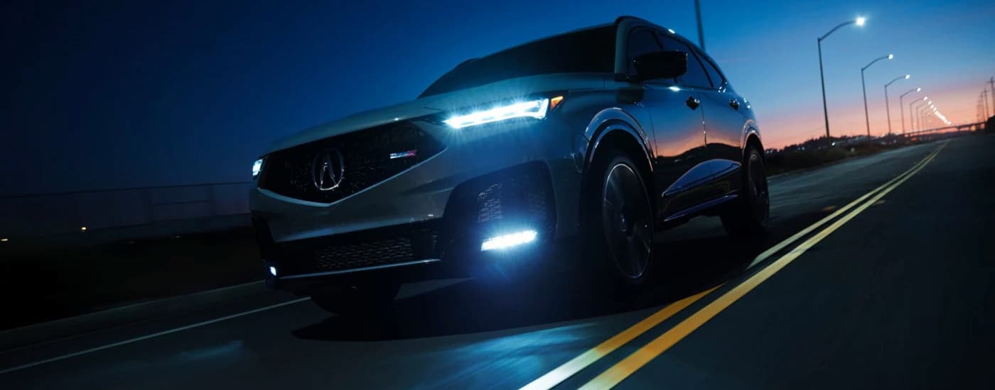 Grey 2026 Acura MDX driving down an open road.