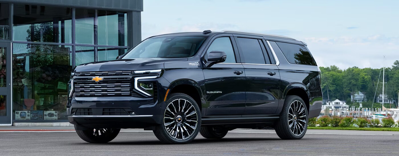 2026%20Chevy%20Suburban%20-%20side.png Black 2026 Chevy Tahoe parked in front of a harbor