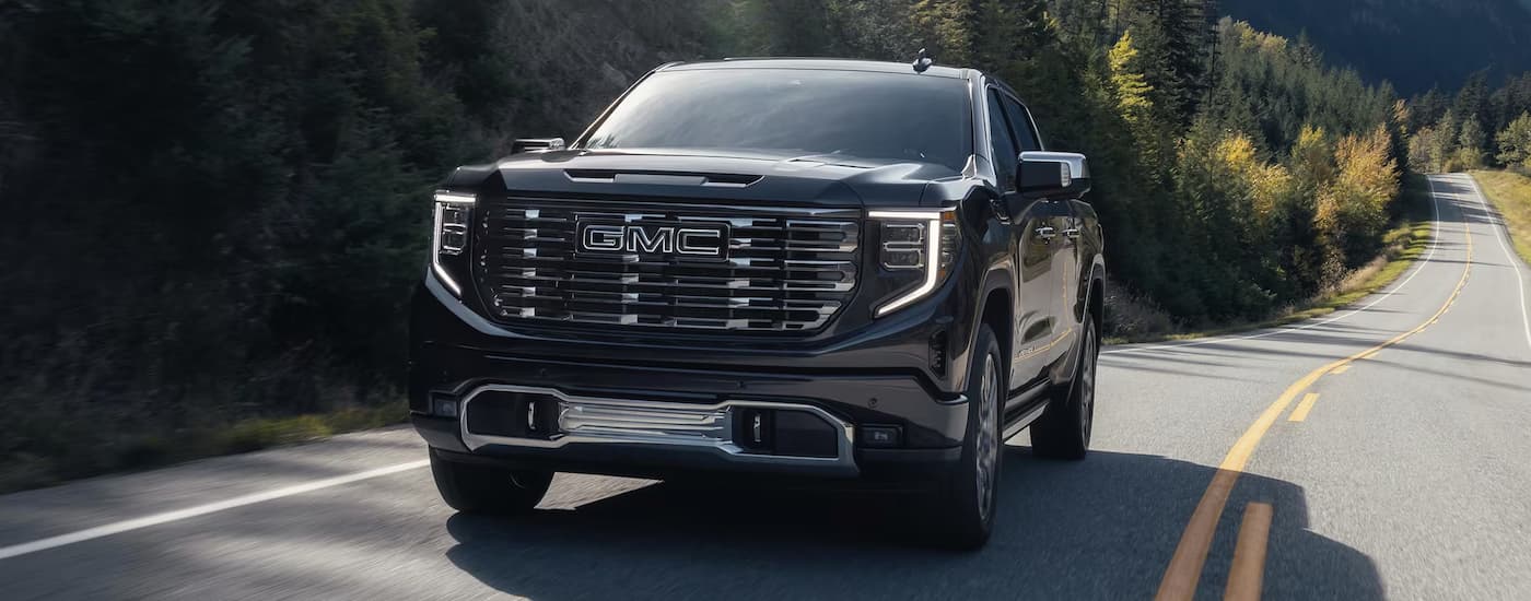 Black 2025 GMC Sierra 1500 Denali Ultimate driving down a road.