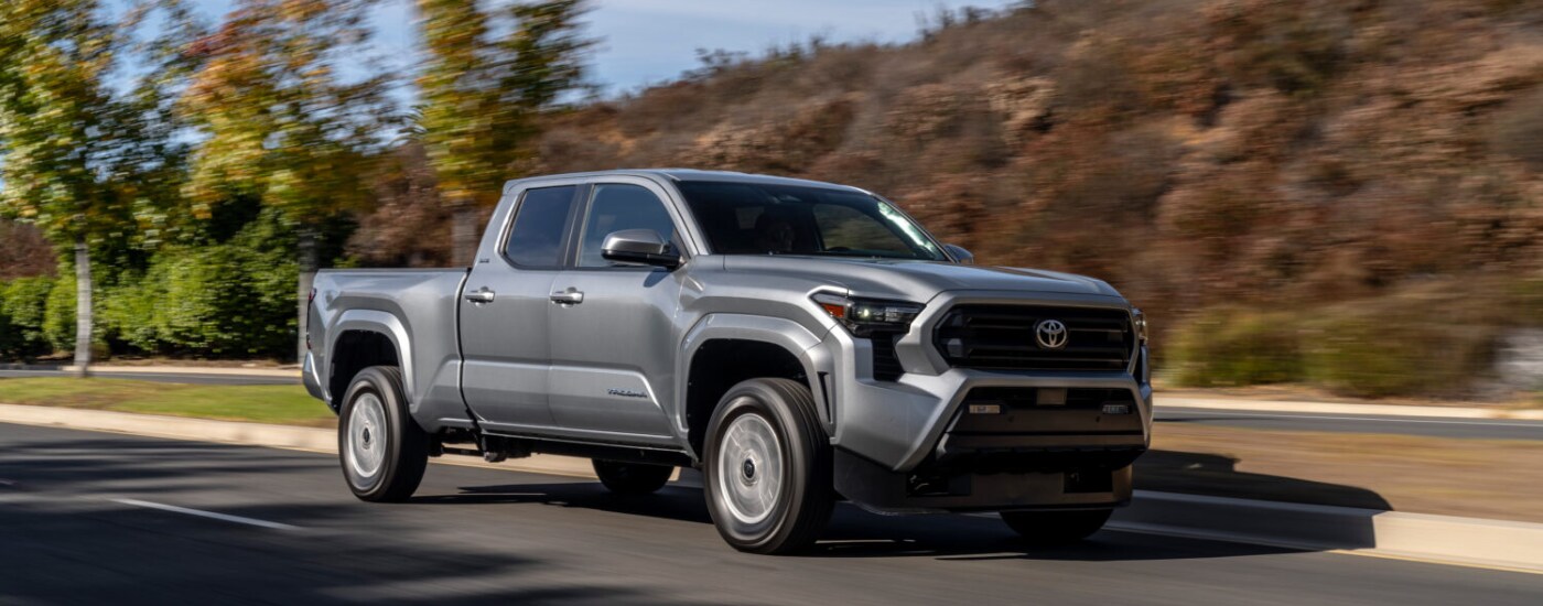 2025%20Toyota%20Tacoma%20-%20Silver.png Silver 2025 Toyota Tacoma driving along an open road