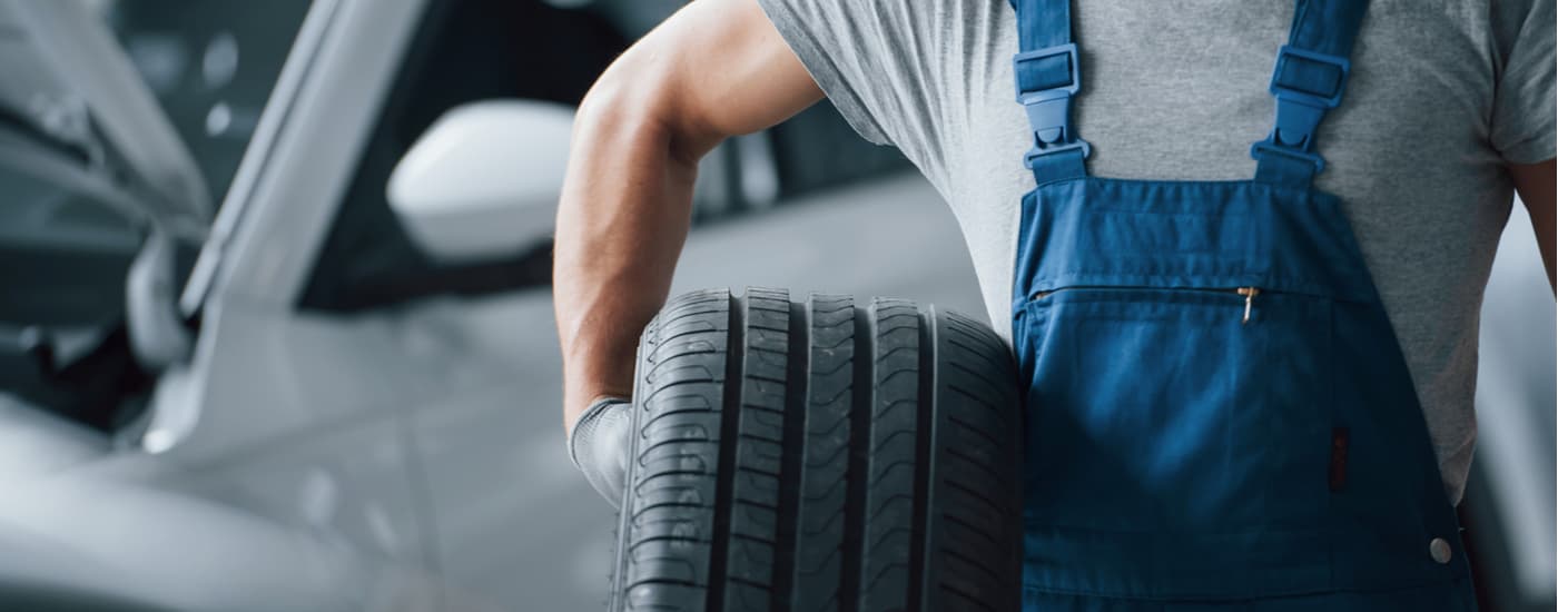 Auto%20Service%20in%20Atlanta%20-%20Mechanic.jpg A mechanic is holding a tire at an auto shop.