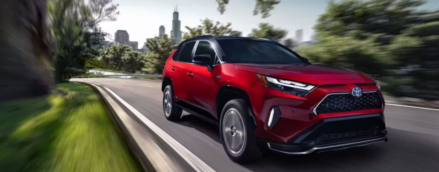 2023%20Toyota%20RAV4%20Prime%20-%20City.jpg A red 2023 Toyota RAV4 Prime is shown driving near a city.