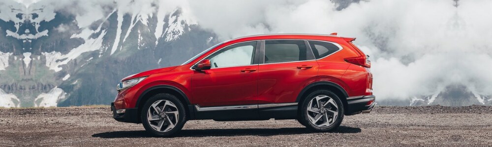 2019 Honda CR-V SUV in Glenwood Springs at Phil Long Honda.png Driver side angle of a red 2019 Honda CR-V SUV parked on a gravel cliff edge overlooking a large snowy mountain top with low sitting clouds