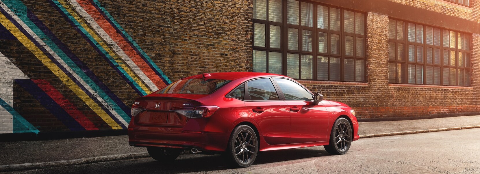 2022 Honda Civic Rallye Red 3.png A red 2022 Honda Civic sits in profile angled view showing the rear of the car as it sits parked on a city street in front of a brick building