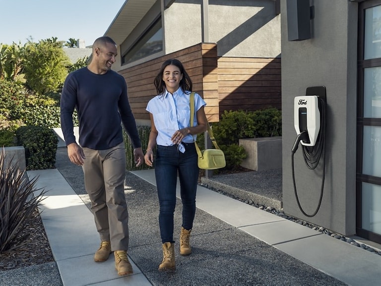 A couple walking out of their home with a Ford Charge Station Pro attached to their garage in the background