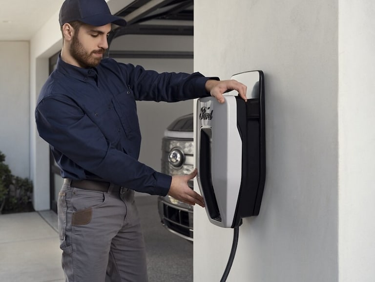 An installer mounting a Ford Charge Station Pro to a wall with a Ford F-150 Lightning® in the garage