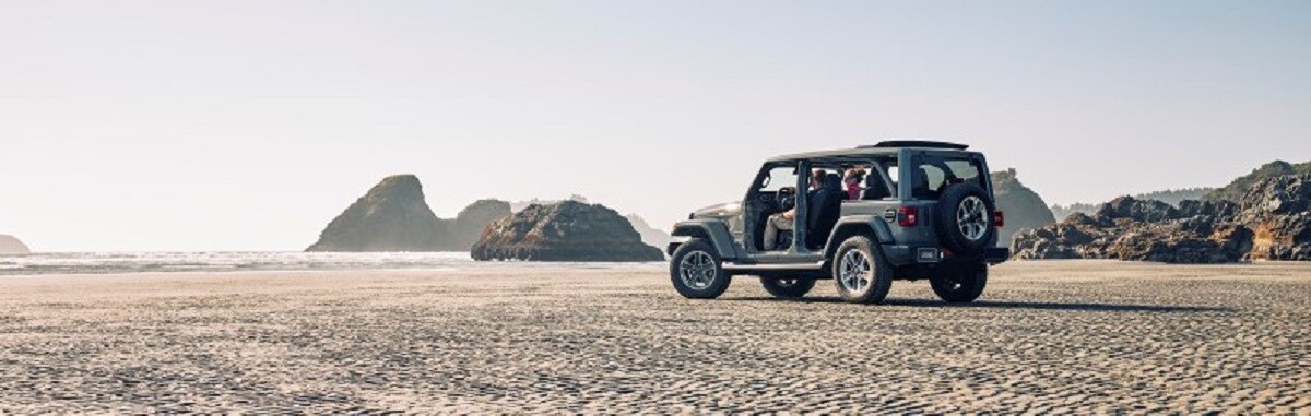 Grey Jeep Wrangler rear drvier side view driving on beach