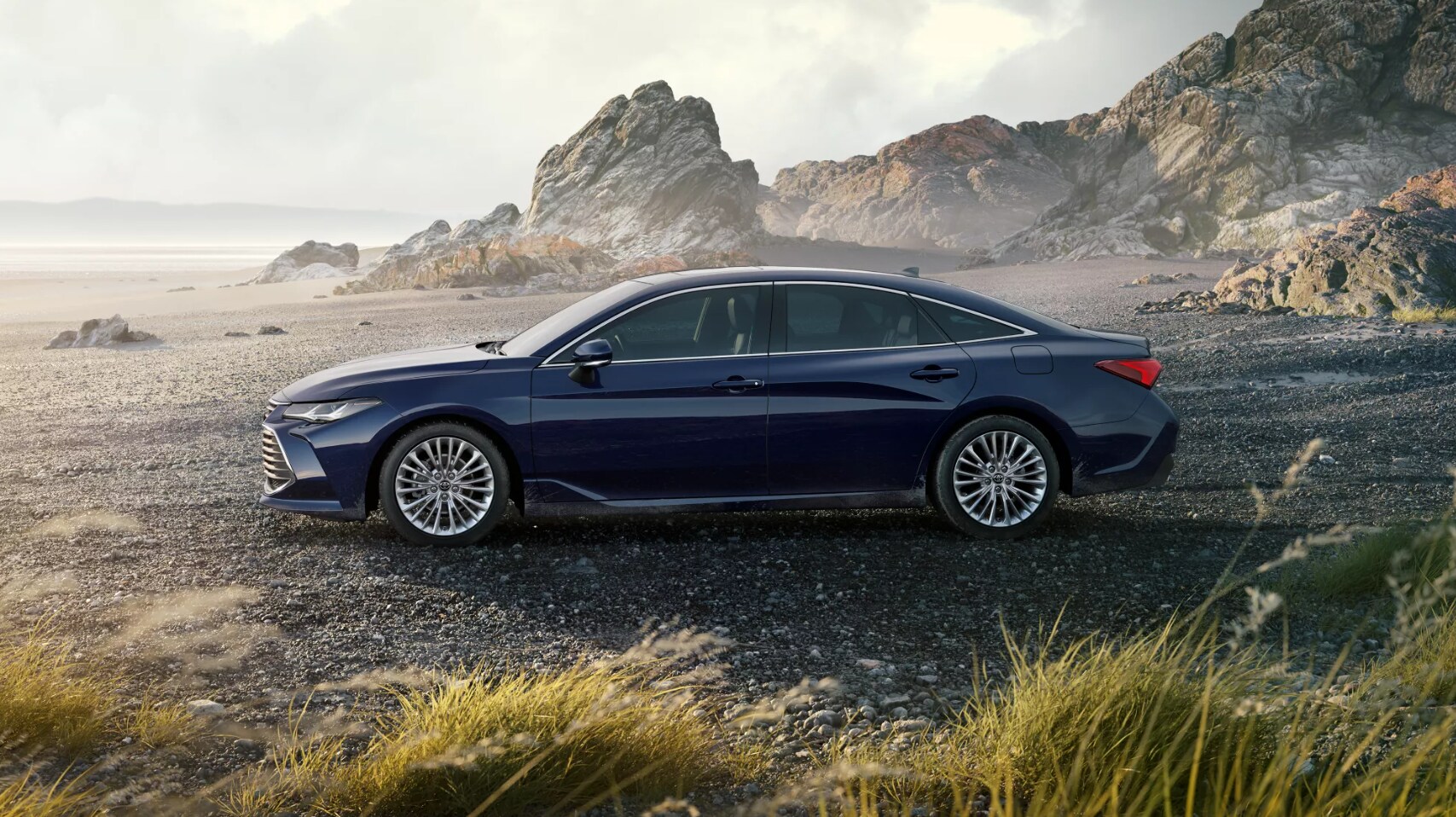 2022-Toyota-Avalon-Hybrid-2.PNG A profile view of a black 2022 Toyota Avalon Hybrid as it sits parked on a rocky beach at sunrise