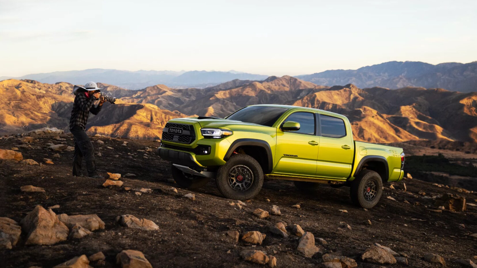 2022-Toyota-Tacoma-1.PNG A lime green 2022 Toyota Tacoma sits parked on a rocky landscape as a photographer stands on the side