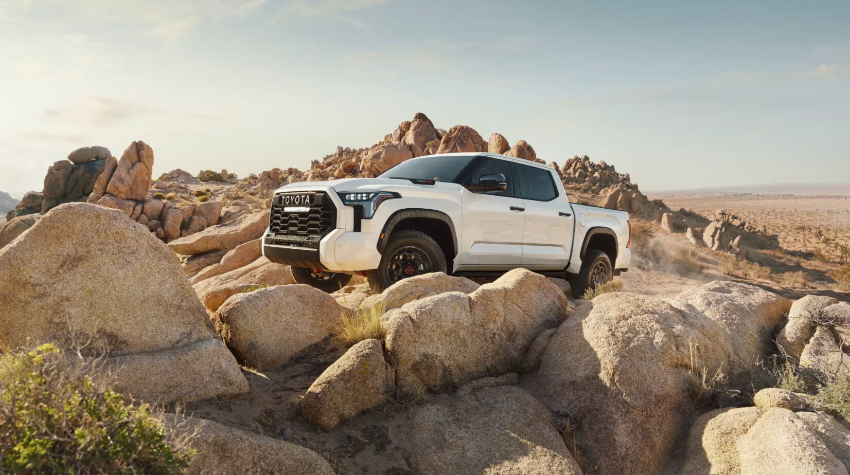 A white 2023 Toyota Tundra sits on a hill of rocks in the desert