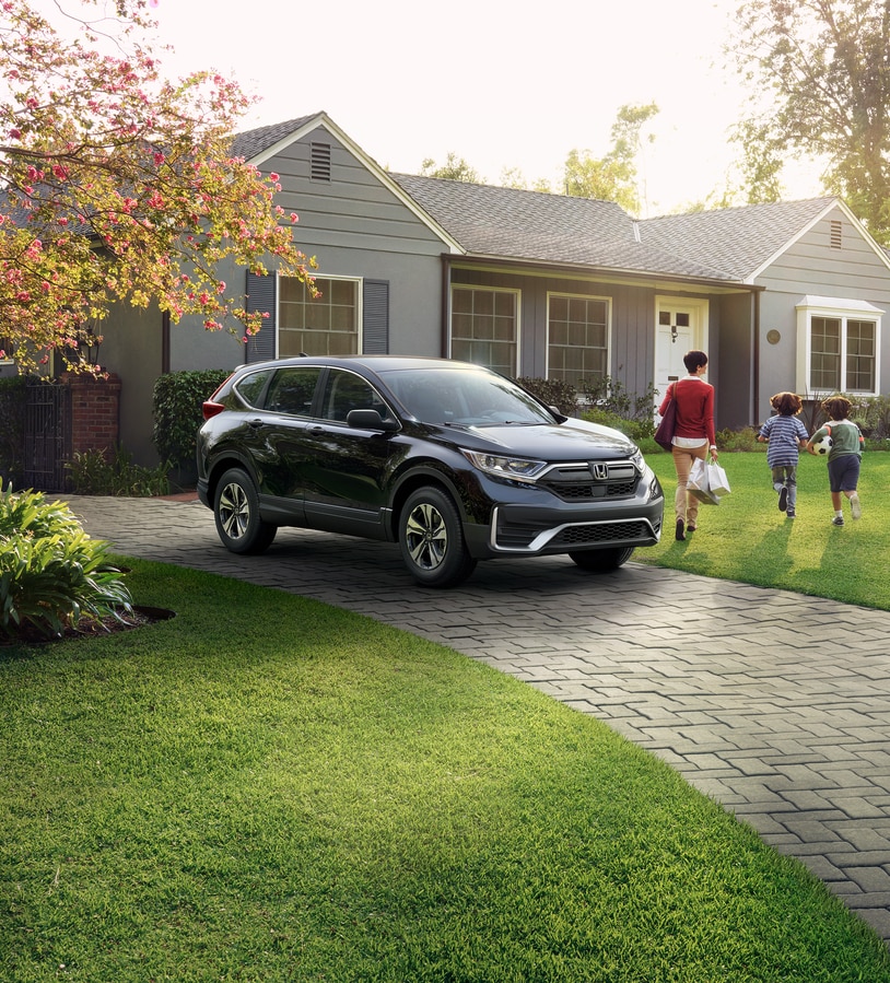 2020-Honda-CRV-LX-SUV.png black Honda CR-V parked in the driveway of a suburban home with a mother and kids walking away