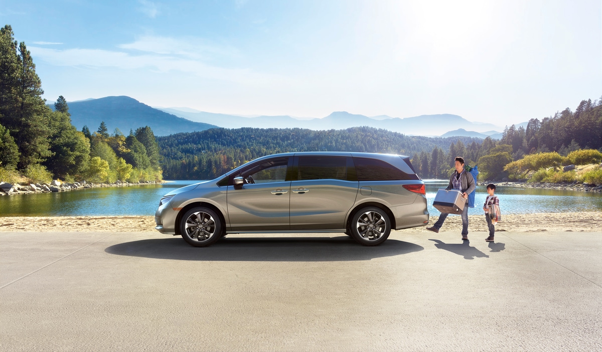 2022-Honda-Odyssey-Elite-Van-L07.png silver Honda Odyssey van parked next to a lake with the driver using hands free tailgate access