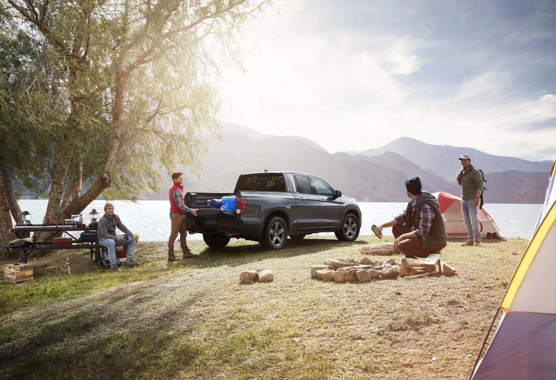 2023 Honda Ridgeline for Sale.png friends sitting around a Honda Ridgeline, parked near a lake, getting camping gear ready