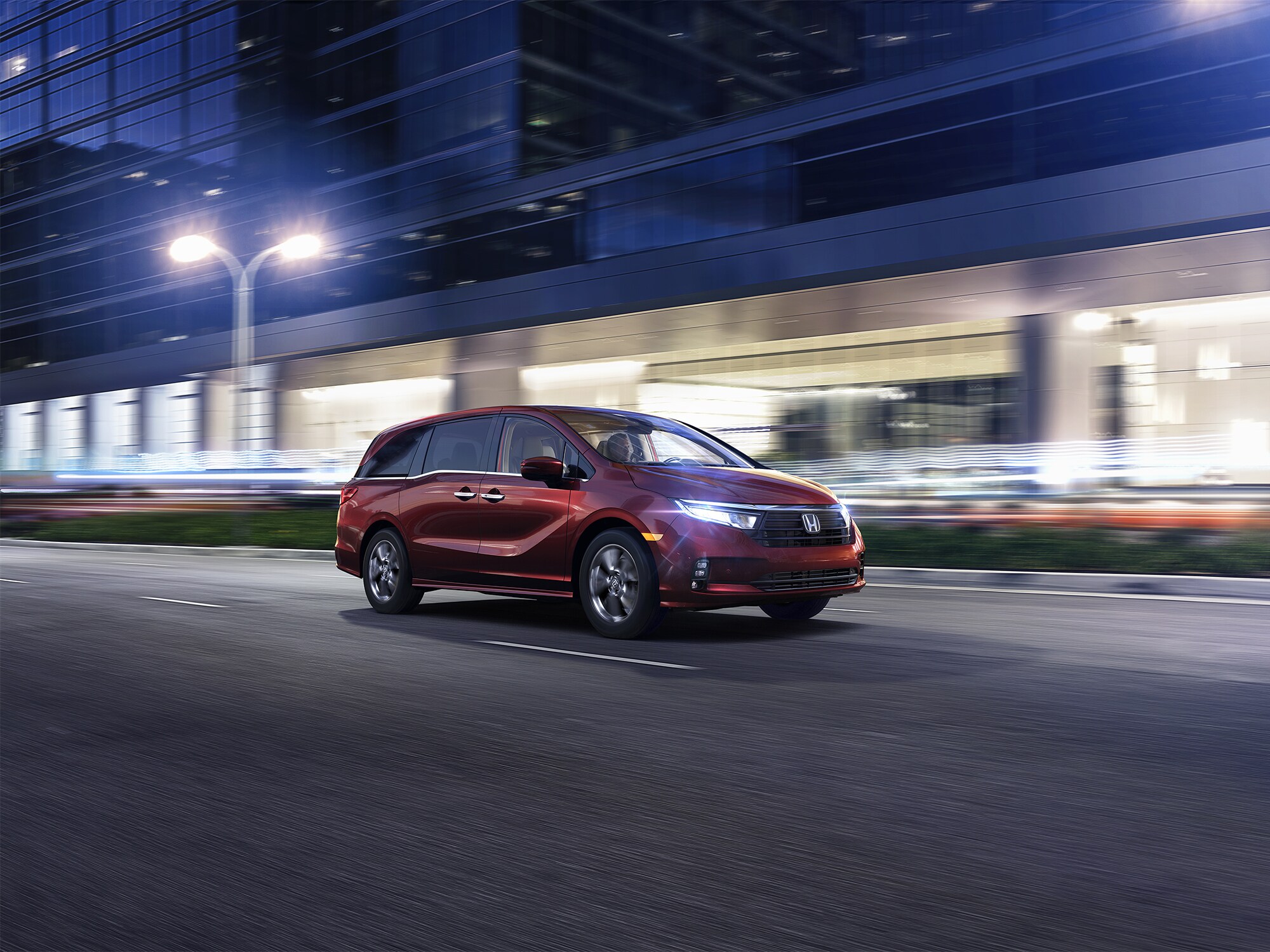 maroon Honda Odyssey driving through a downtown area at night