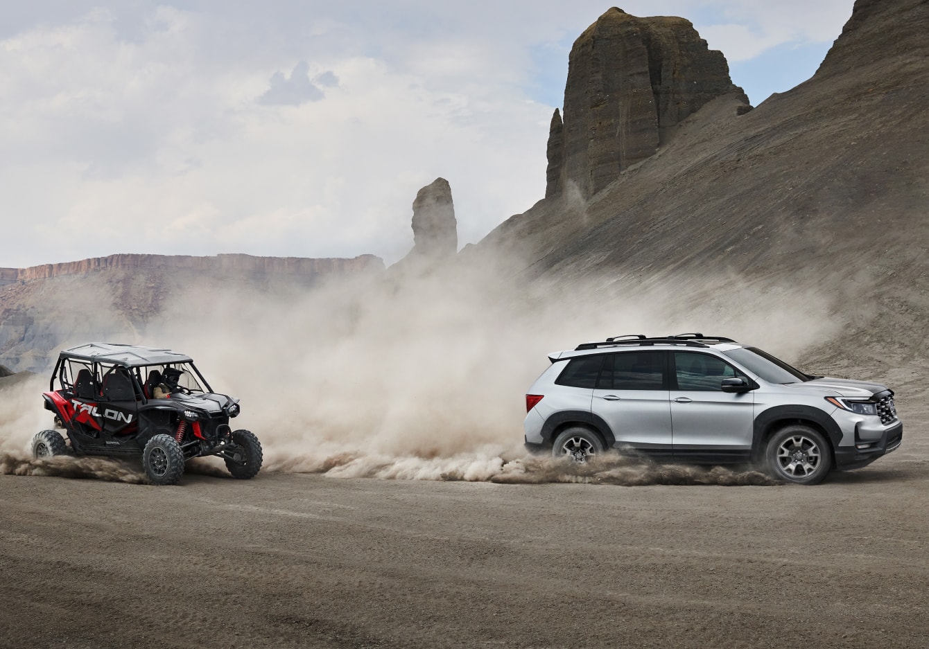 silver Honda Passport driving in the sand with an ATV behind